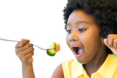 Close up portrait of little girl taking a bite of broccoli and carrot.