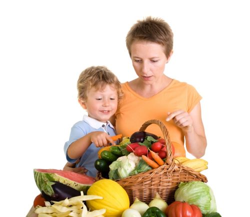 small boy and his mother in front of different vegetables