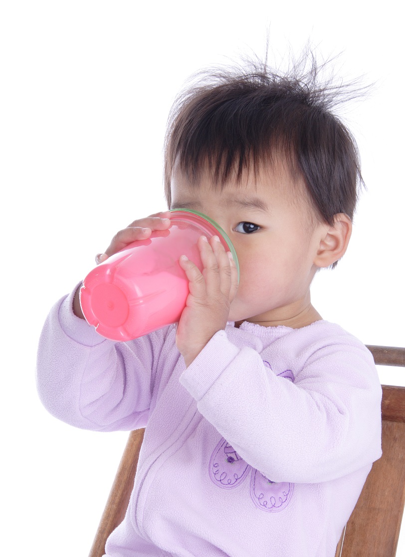 An eighteen-month old drinks milk from a sippy cup.