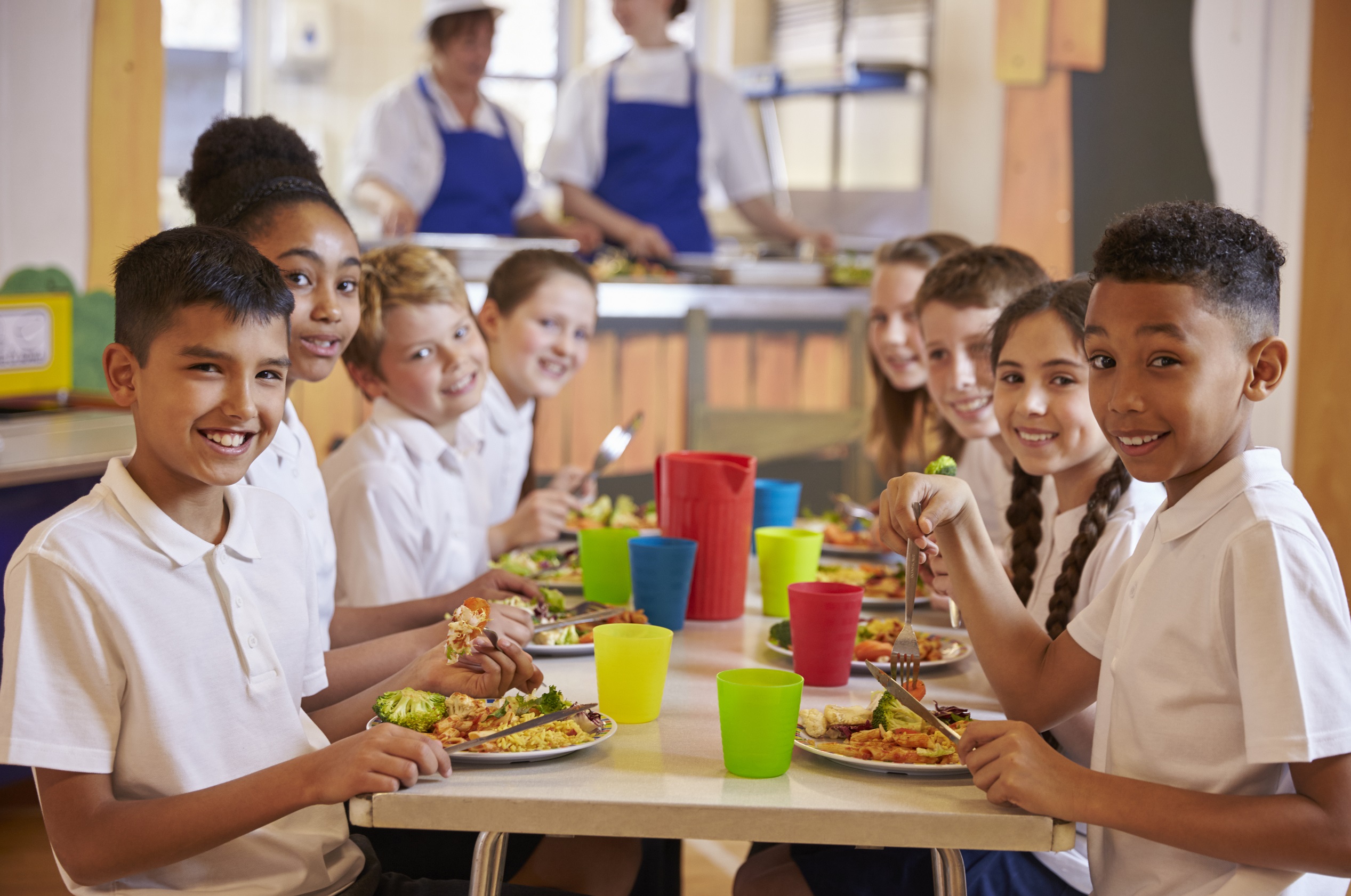 Kids at a table in a primary school cafeteria look to camera