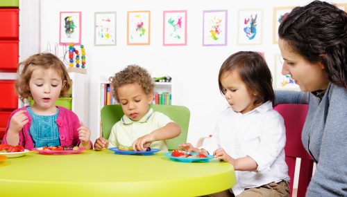 A protrait of a carer superving a group of little children at mealtime.